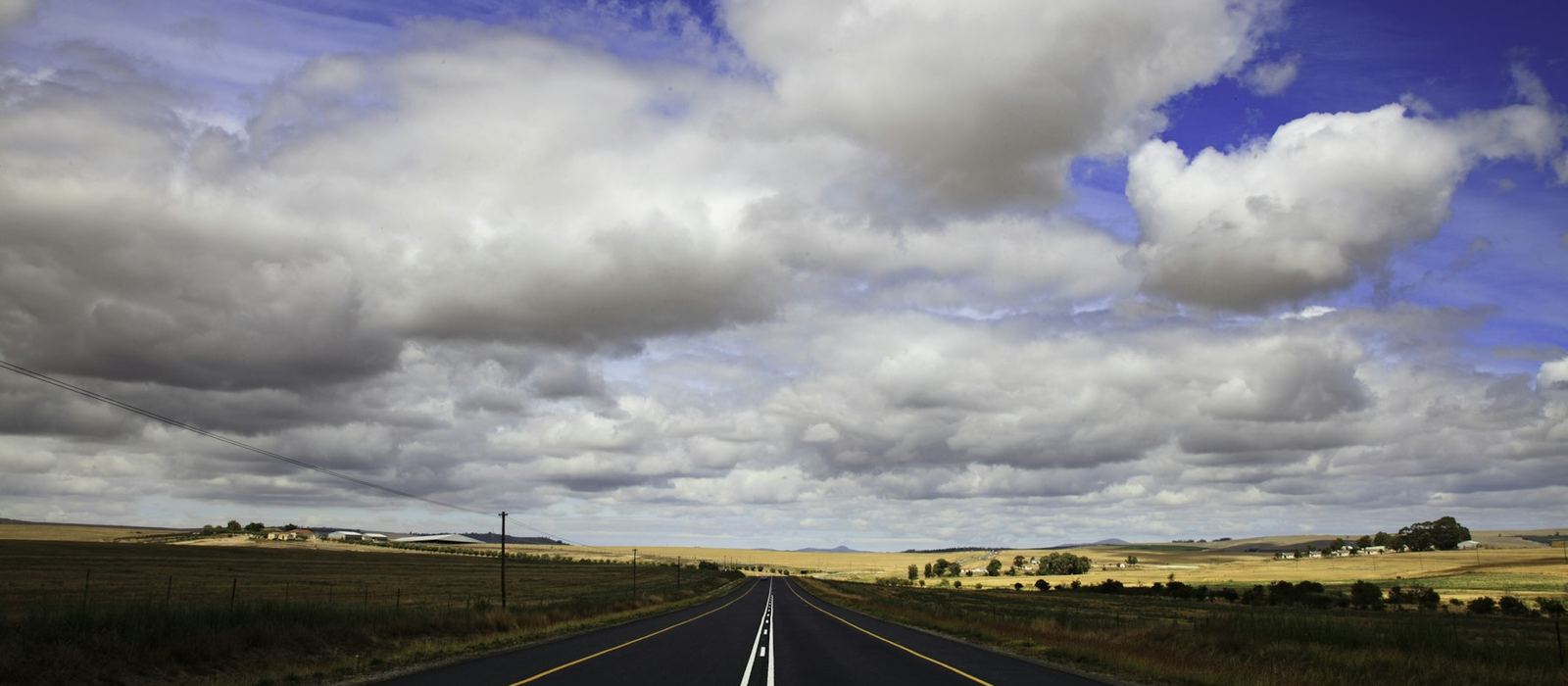 An open road running to the horizon under a wide, cloud-filled sky