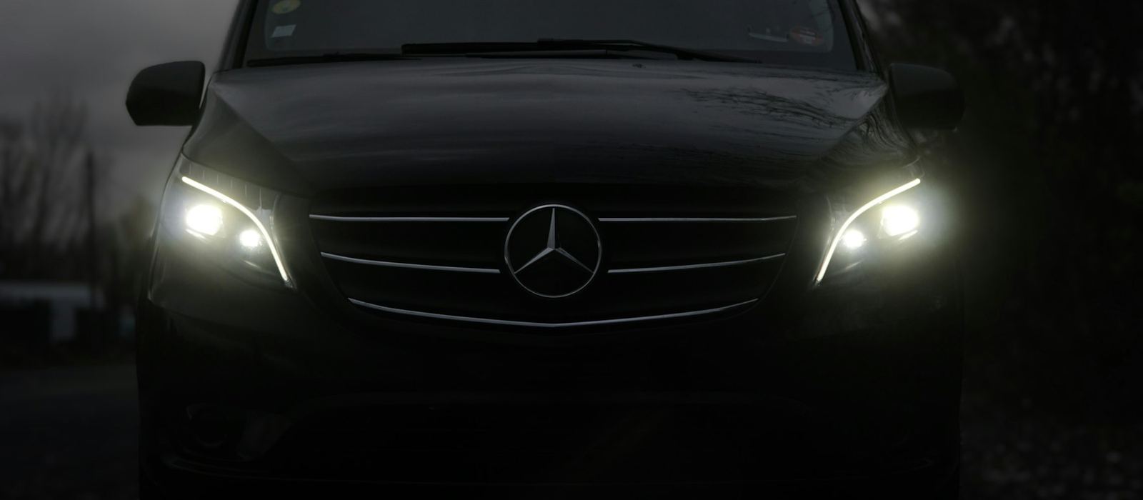 A dark executive people-carrier photographed head-on with its headlights on