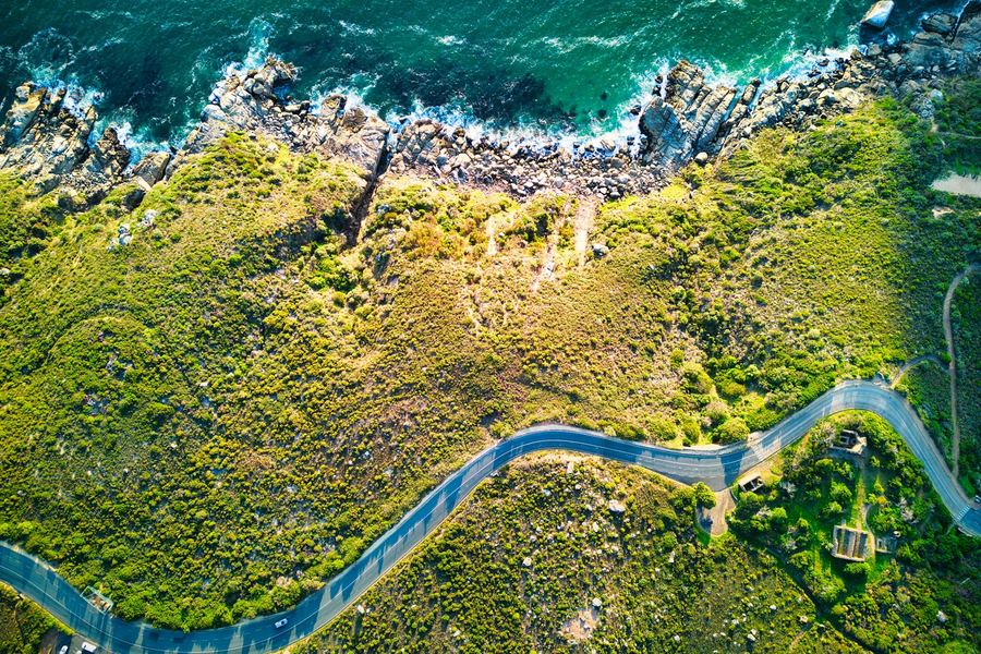 An aerial view of a coastal road winding between green hills and the sea
